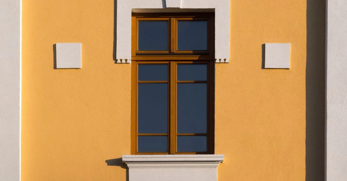Une fenêtre minimaliste sur un mur orange vif projetant des ombres audacieuses, idéale pour les projets architecturaux.