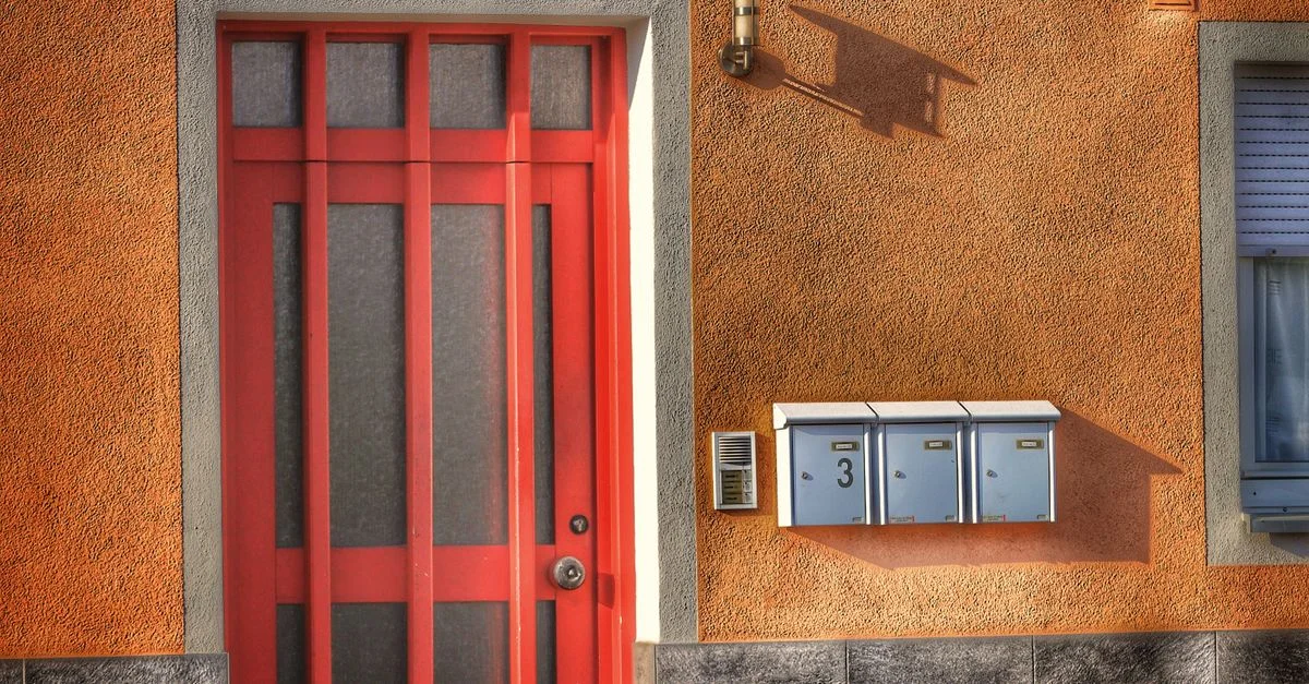 Porte rouge vif avec boîtes aux lettres sur un mur orange texturé, design moderne.