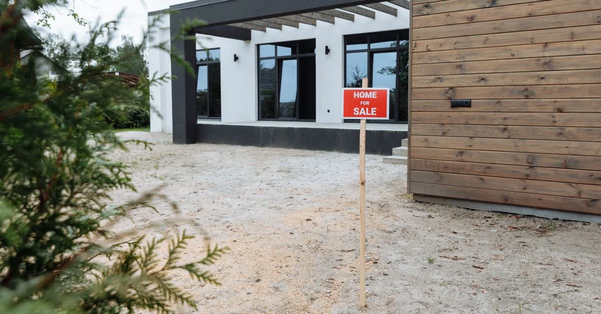 Extérieur moderne d'une maison avec un panneau 'Maison à vendre' dans le jardin.
