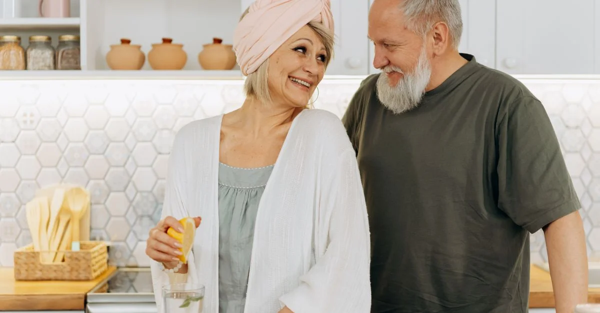 Couple senior souriant préparant du jus frais dans une cuisine confortable.