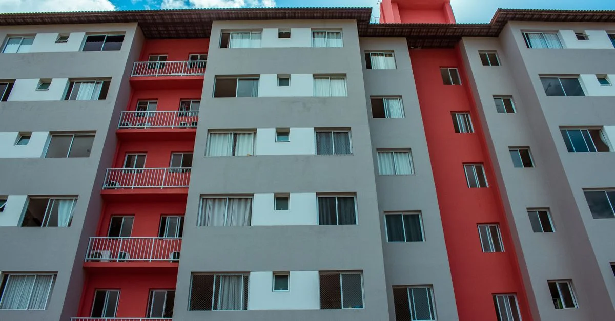 Un immeuble résidentiel de grande hauteur avec une façade rouge frappante et des balcons sous un ciel bleu.