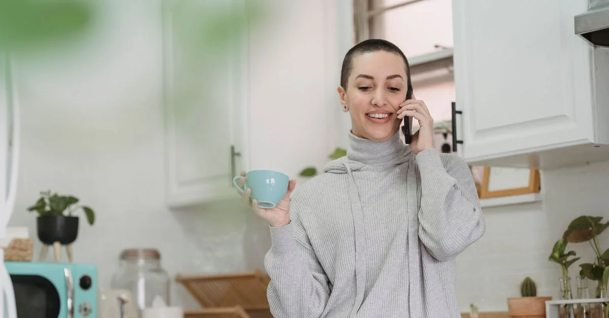 Femme souriante dans une cuisine confortable buvant du café et parlant au téléphone.