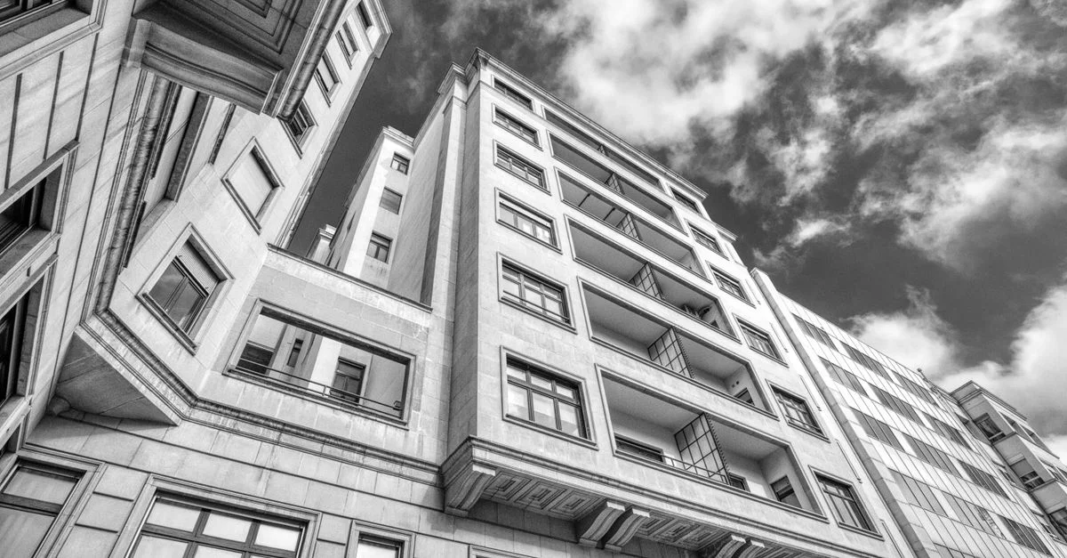 Vue en contre-plongée de bâtiments d'appartements urbains avec un ciel dramatique en noir et blanc.